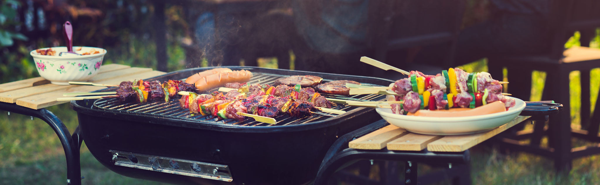 A grill cooking hot dogs, burger patties, and skewers of meat and vegetables.